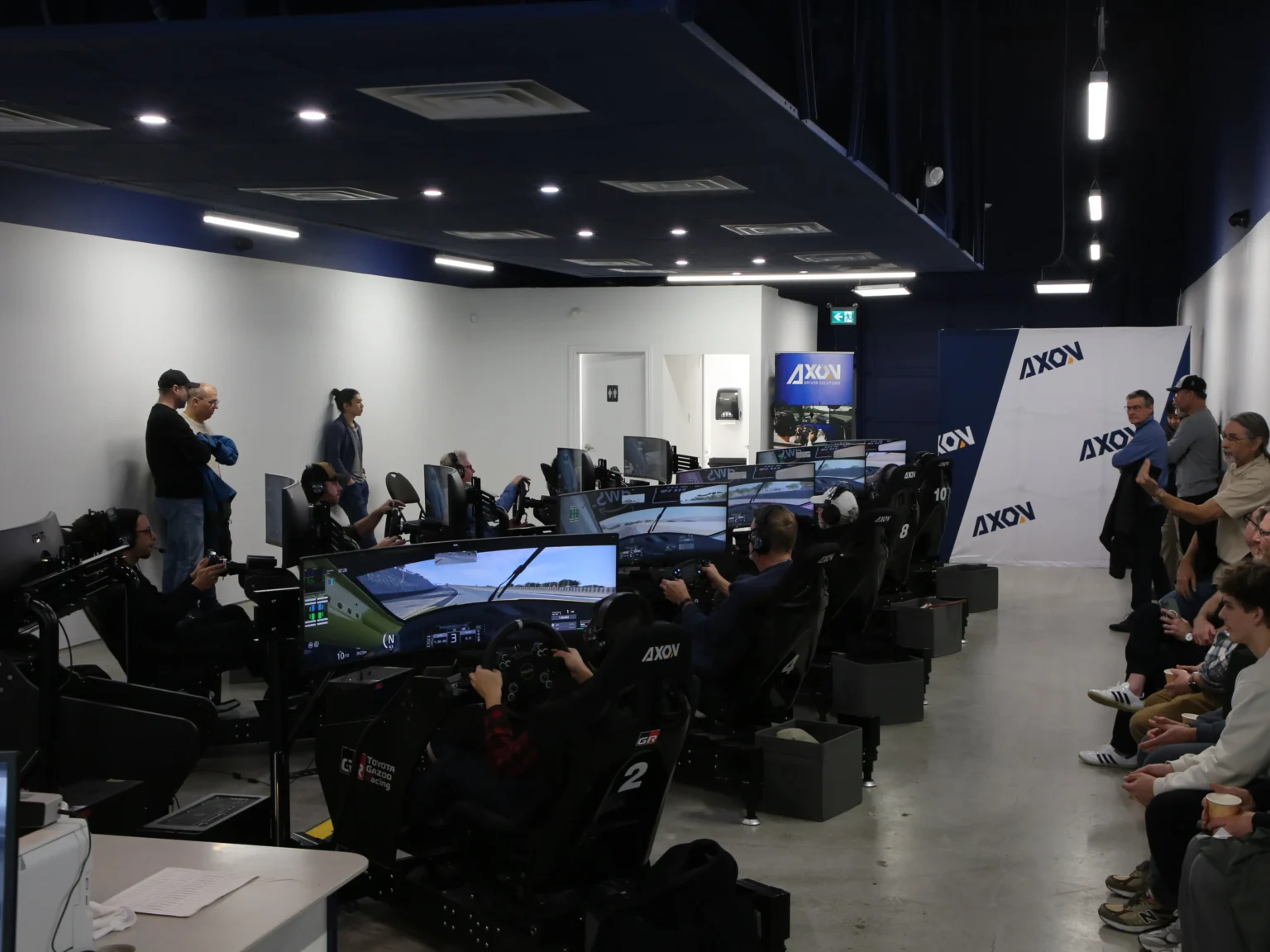 The Axon sim centre floor in Richmond, a full row of simulators in use with spectators watching